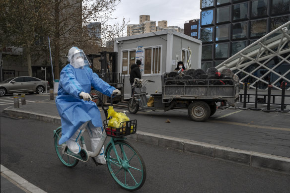 An epidemic control worker wears PPE as she passes workers as they prepare to remove a COVID-testing booth in Beijing.  