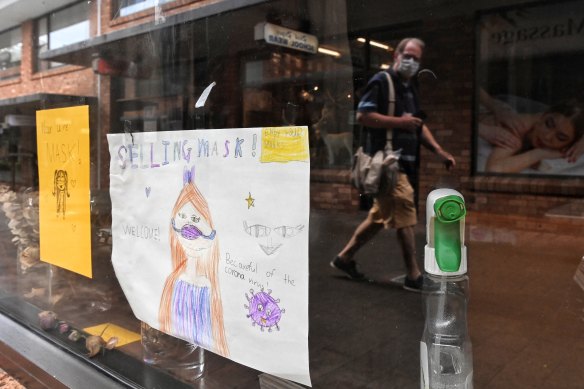 A child's drawing on a window shop encourages shoppers to buy and wear masks.