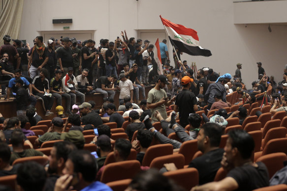 Iraqi protesters pose with national flags, inside the Parliament building in Baghdad, Iraq, pm Saturday, July 30.