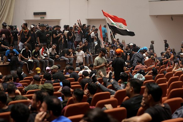 Iraqi protesters pose with national flags, inside the Parliament building in Baghdad, Iraq, pm Saturday, July 30.