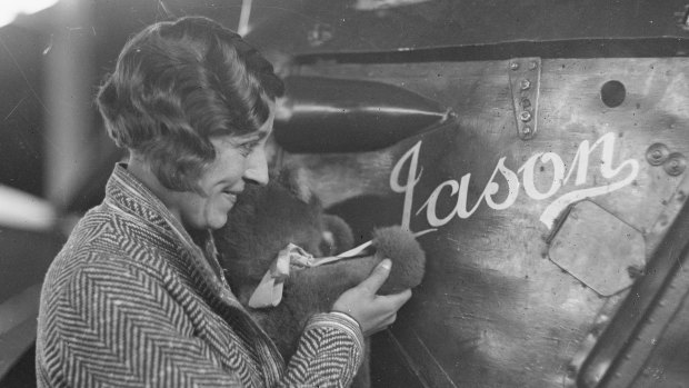 Amy Johnson holding a teddy bear, at Mascot, Sydney with her Gipsy Moth plane "Jason" ca 1930.