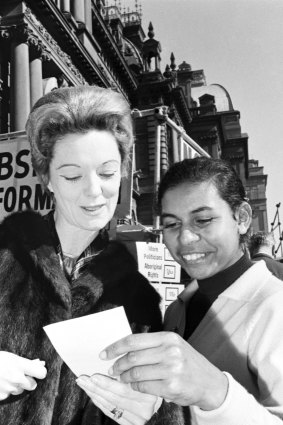 A young Aboriginal girl hands a how to vote card to a voter at polling booth at Sydney Town Hall during the 1967 referendum.