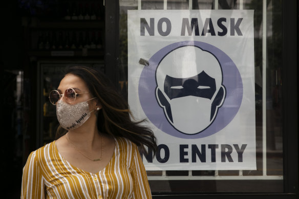 A woman walks out of a liquor store past a sign requesting customers wear a mask in Santa Monica, California. 
