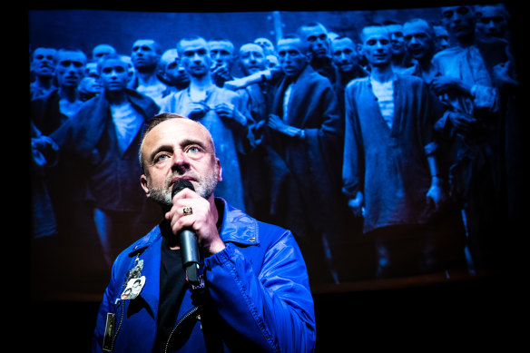 In his work Truth to Power Cafe, Jeremy Goldstein stands in front of an image of Ebensee, a sub-camp of the Mauthausen concentration camp in Austria.