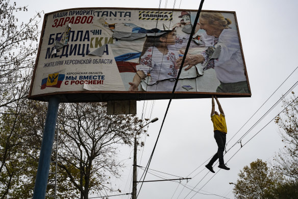 A Ukrainian man hangs off to tear down a billboard with the slogan “We are together with the Russian government!” in the recently liberated city of Kherson, Ukraine, on Sunday, November 13.