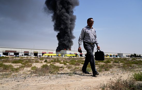 A man walks away after watching a black plume of smoke rising from a warehouse in the industrial area of Sharjah City, United Arab Emirates.
