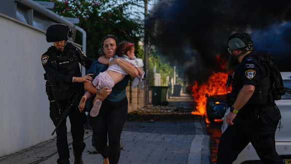 Police officers evacuate a woman and a child from a site hit by a rocket fired from the Gaza Strip, in Ashkelon, southern Israel, Saturday, Oct. 7, 2023. The rockets were fired as Hamas announced a new operation against Israel.