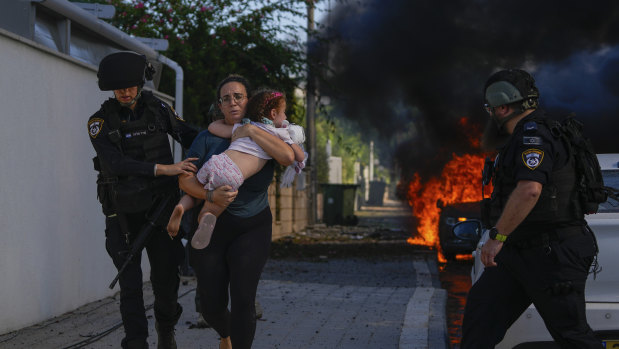 Police officers evacuate a woman and a child from a site hit by a rocket fired from the Gaza Strip, in Ashkelon, southern Israel, Saturday, Oct. 7, 2023. The rockets were fired as Hamas announced a new operation against Israel.