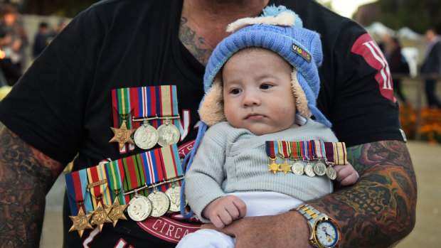 Baby Tyson observes the Anzac Day proceedings from the arms of his father Corey Van Wyngaarden. 