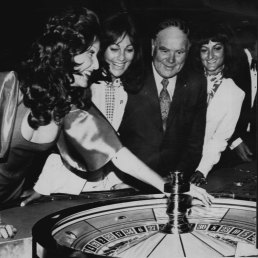 “Tasmania’s Premier, Mr Reece, sets the ball rolling at Wrest Point. With him are croupier Honey Hogan (left) and tw woman guests.”