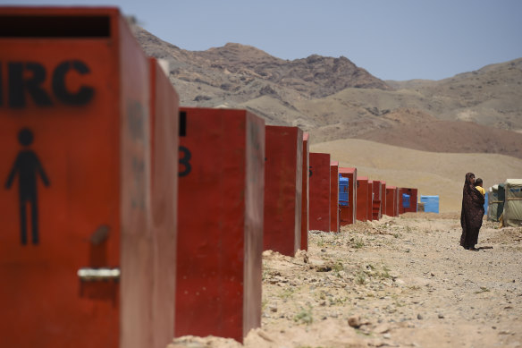 Passing a row of toilets, Ziba aged 21 years walks back to her family’s temporary shelter in Regreshan camp.