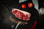 Raw ribeye beef steak cooking with ingredients on a black plate. Top view.
