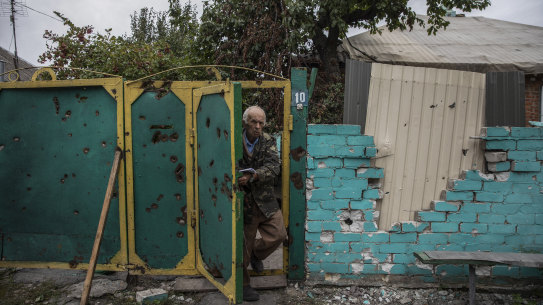 An elderly man wearing a military coat steps outside the damaged gate of his home in the liberated village of Zaliznychne, Ukraine on September 11, 2022. 