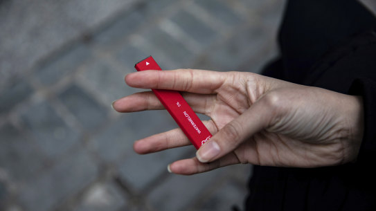 A woman holds a flavoured disposable vape device.