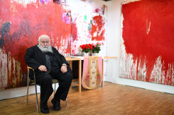 Austrian artist Hermann Nitsch sits in front of his artworks at an exhibition in 2018.