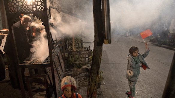 A Uighur child holds up a Chinese national flag near a vendor barbecuing skewered lamb meat in Kashgar in western China's Xinjiang region.