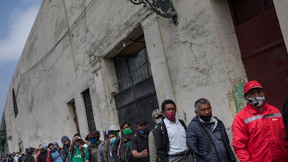 People wearing masks to curb the spread of the new coronavirus wait for food outside the San Francisco de Asis soup kitchen which is handing out food for the homeless and poor in Lima, Peru.