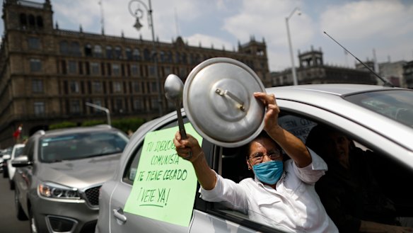 A woman bangs a pot lid next to a sign reading in Spanish; "Your communist ideology is blinding you, leave already!" during a protest calling for Mexican President Andres Manuel Lopez Obrador to step down.