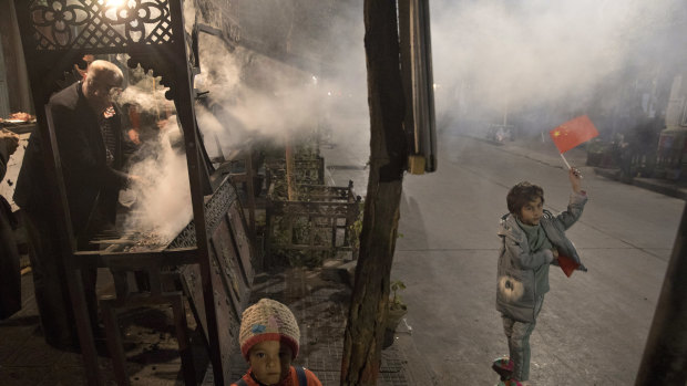 A Uighur child holds up a Chinese national flag near a vendor barbecuing skewered lamb meat in Kashgar in western China's Xinjiang region.