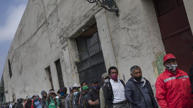 People wearing masks to curb the spread of the new coronavirus wait for food outside the San Francisco de Asis soup kitchen which is handing out food for the homeless and poor in Lima, Peru.