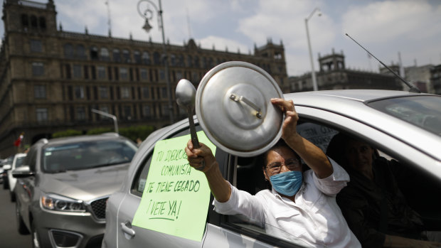 A woman bangs a pot lid next to a sign reading in Spanish; "Your communist ideology is blinding you, leave already!" during a protest calling for Mexican President Andres Manuel Lopez Obrador to step down.