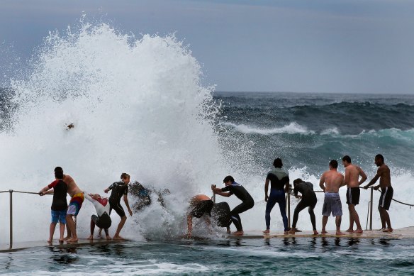 A regular scene at Bronte beach: teenagers cling onto the railing as large waves break over the top of them.