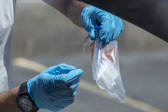 A healthcare worker shows a resident how to complete a COVID-19 spit test at a Utah County Health Department drive-thru testing site in American Fork, Utah.