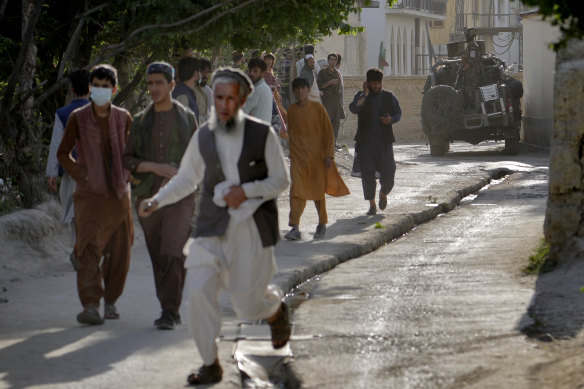 People leave the site of an explosion as a Taliban fighter stands guard in Kabul.