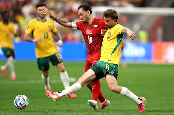 Connor Metcalfe #8 of Australia passes the ball under pressure from Hakan Calhanoglu.