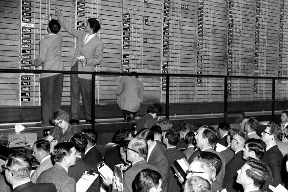 Officials chalk share prices on the elevated post board at the new premises of the Sydney Stock Exchange. 