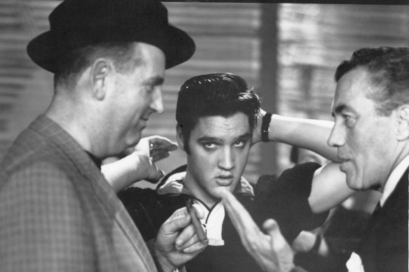 Colonel Parker (left) talks with TV host Ed Sullivan, while Elvis grooms himself backstage at Sullivan’s television show in October 1956.