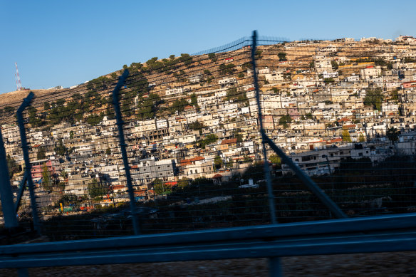 Israeli settlements sit behind a wire security fence along a road outside of Hebron in the West Bank in December 2023.