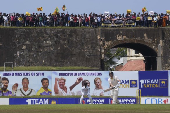 Steve Smith bats while protesters converge atop the Dutch fort behind the Galle stadium.