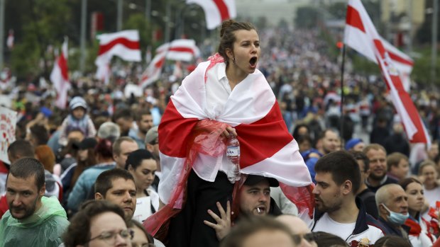 A woman covers herself by an old Belarusian national flag reacts as opposition supporters gather in front of police line toward the Independence Palace, residence of the President Alexander Lukashenko in Minsk, Belarus.