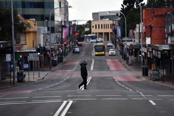 A lone person walks across Moore Street, Liverpool on Saturday as Sydney bunkers down under tightened restrictions announced by Premier Berejiklian on Friday. 