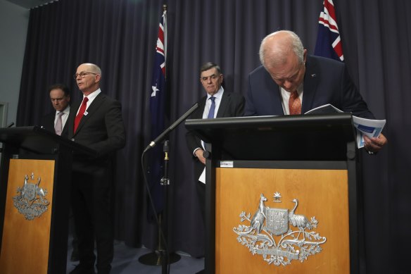 (From left) Greg Hunt, Professor Paul Kelly and Professor Brendan Murphy with Prime Minister Scott Morrison, who is taking a closer look at his notes during a press conference on Thursday night.