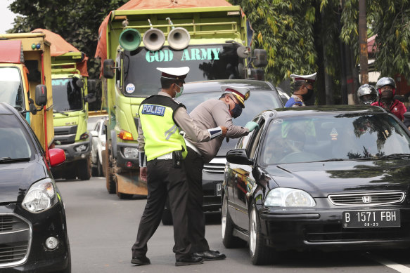 Police officers check the number of people seated inside a car at a checkpoint in Jakarta during the imposition of large-scale social restriction.
