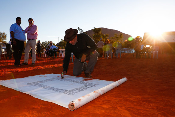 Noel Pearson signs a canvas on which the Uluru Statement from the Heart, which included the proposal for a Voice to Parliament, was later painted in May 2017.