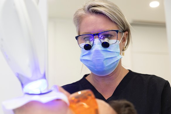 Dental hygienist Charmaine Maher watches as the peroxide takes effect on Carre’s teeth.