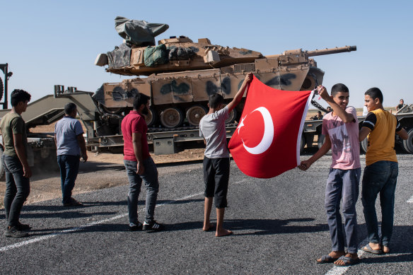 People hold a Turkish flag as they give their support to the Turkish military during the deployment of tanks to Syria on October 12, in Akcakale, Turkey. 