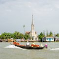 Traditional wooden boats cross the Mekong with Cai Be church in the background.