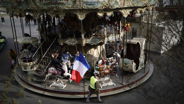 A man carrying a French national flag walks past a carousel near Sacre Coeur in Paris, on Saturday.