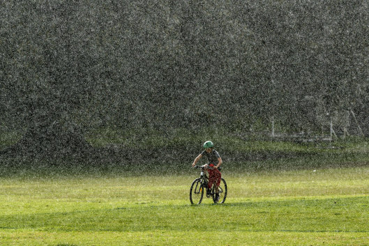 A cyclist rides through heavy rain at Queens Park in mid-2020.