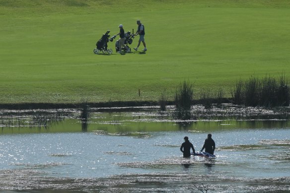 Golfers walk past as police retrieve a body from the water at The Lakes Golf Club on Wednesday morning.