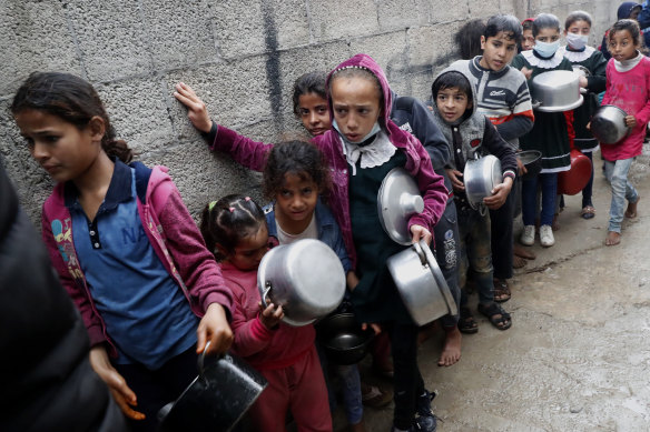 Palestinian children wait in line while holding pots to receive free meals of green pea stew cooked by Samera Abu Amra, unseen,  for distribution to poor residents in Gaza City on Thursday.