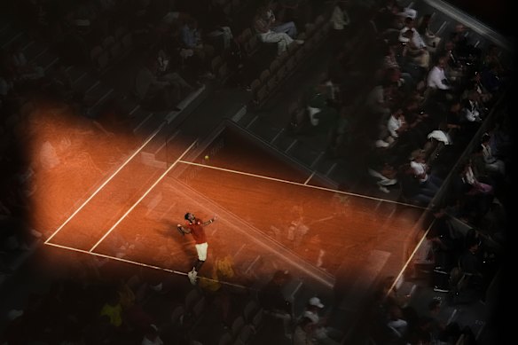 Fans are reflected in glass as Gael Monfils serves during a second-round match of the French Tennis Open at the Roland-Garros stadium in Paris.