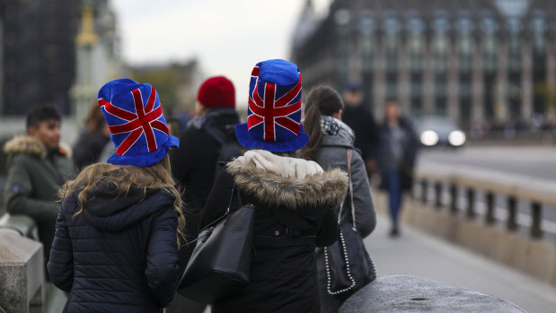 Tourists wearing a hat featuring the design of a British Union flag, also known as a Union Jack, walk over Westminster Bridge in London.