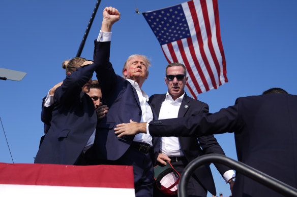 A bloody former president Donald Trump gestures as he is surrounded by Secret Service agents.