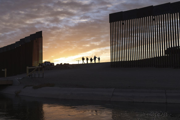 A pair of migrant families from Brazil passes through a gap in the border wall to reach the United States after crossing from Mexico in Yuma, Arizona. 