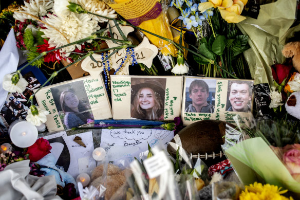  Photographs of four students — Hana St. Juliana, 14; Madisyn Baldwin, 17; Tate Myre, 16; and Justin Shilling, 17 — sit among bouquets of flowers, teddy bears and other personal items left at the memorial site in December 2021.